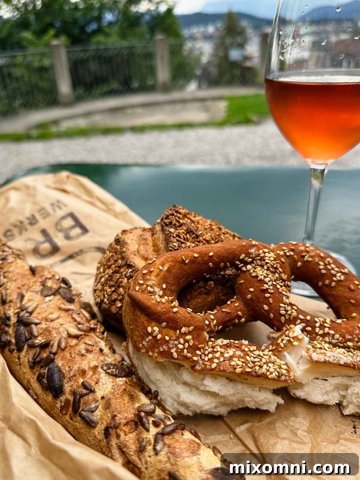 A soft pretzel and a slice of artisanal gluten-free bread resting on a stone wall, accompanied by a glass of chilled rosé wine, capturing a delightful culinary moment in Switzerland.