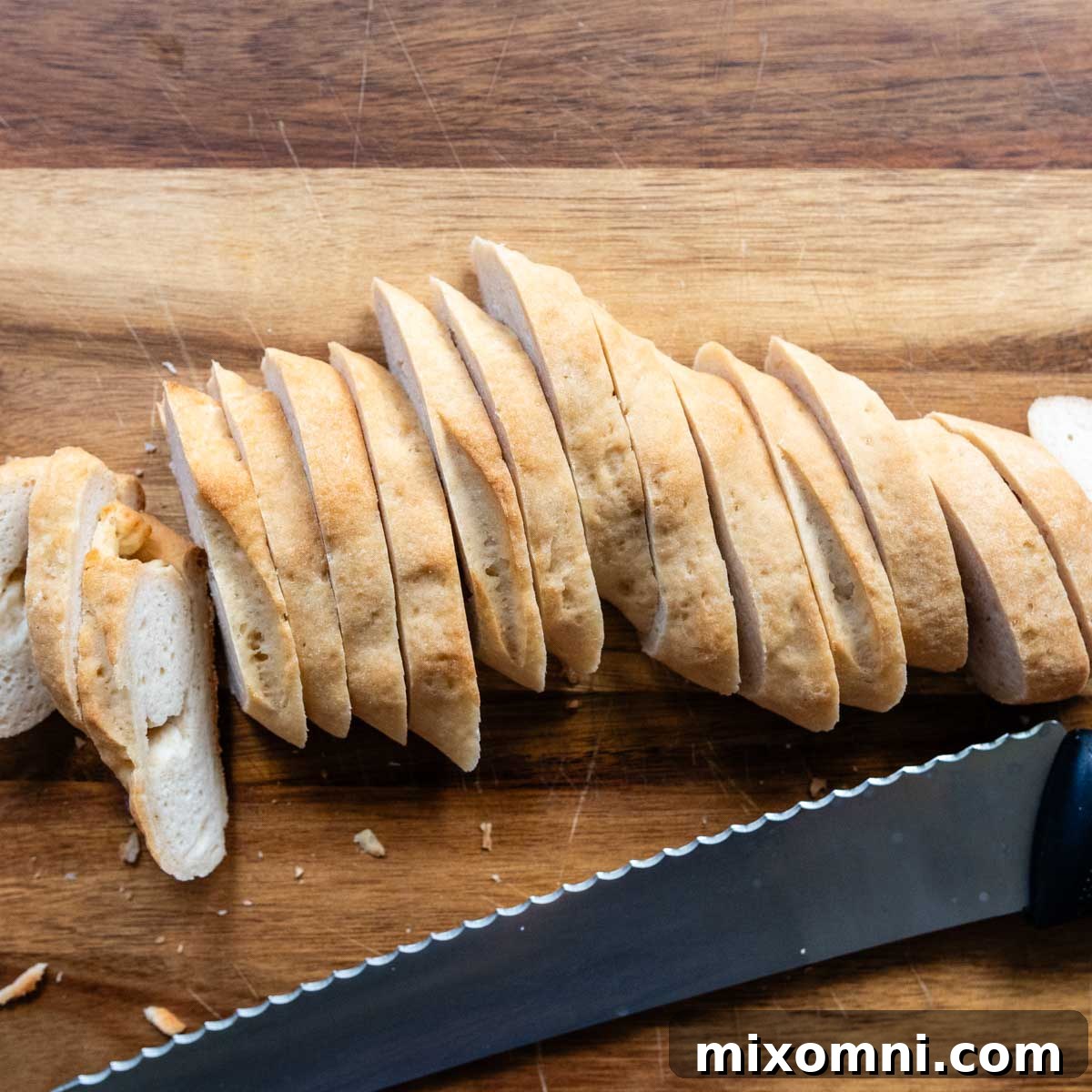 A gluten-free baguette sliced diagonally on a wooden cutting board, ready for seasoning.