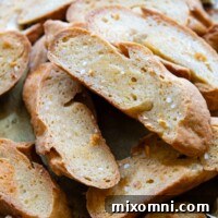 A close-up of perfectly toasted gluten-free crostini piled high, with fresh garlic in the background.