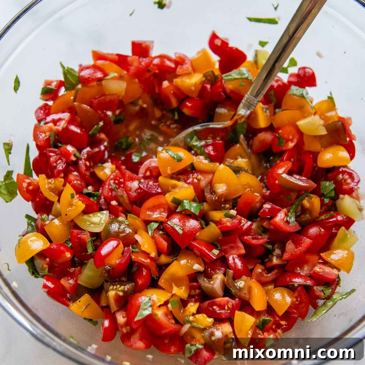 a large bowl with diced tomatoes and fresh basil being stirred.