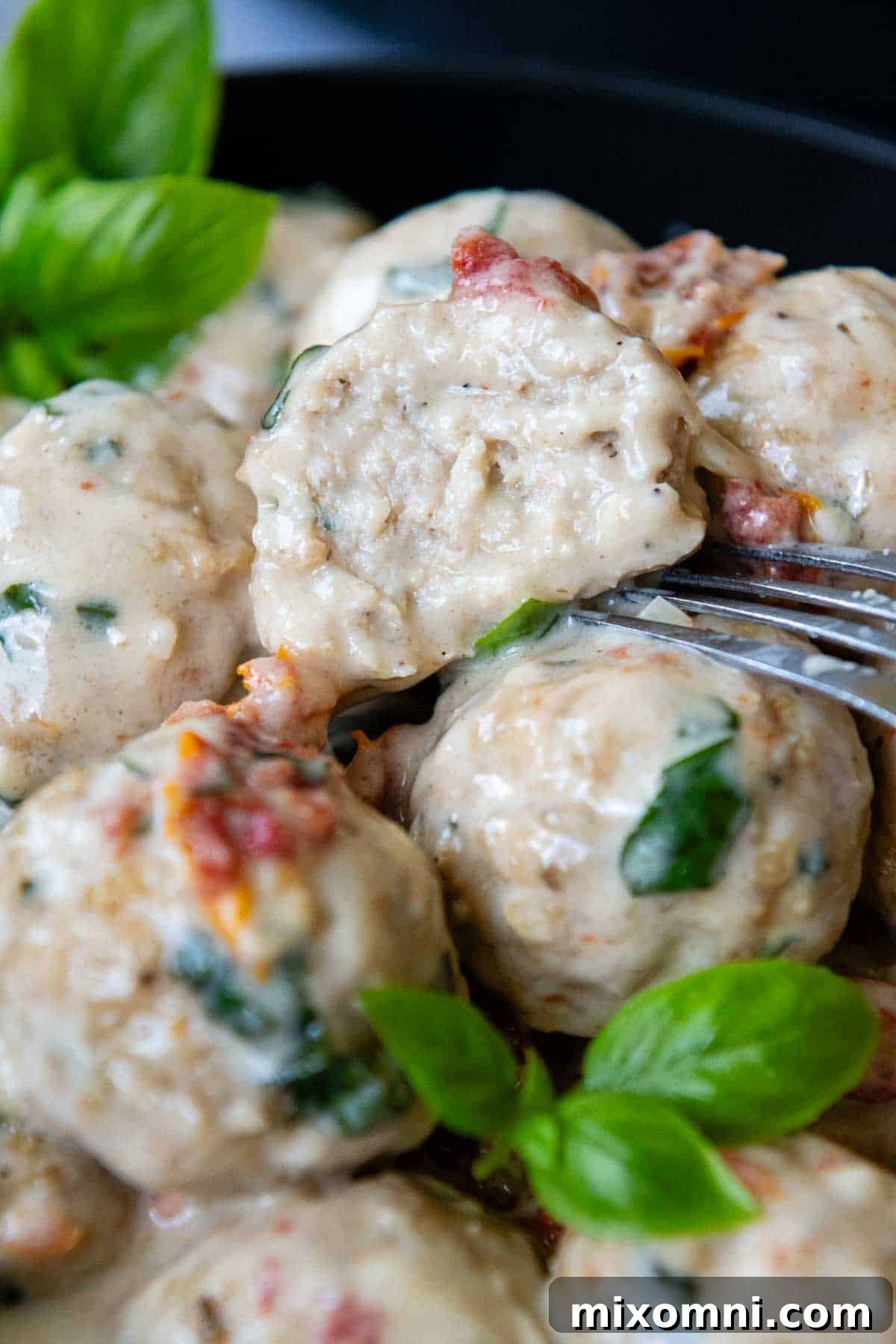 A perfectly cooked gluten-free chicken meatball, cut in half to reveal its moist interior, with a fork resting beside it in a rustic setting.