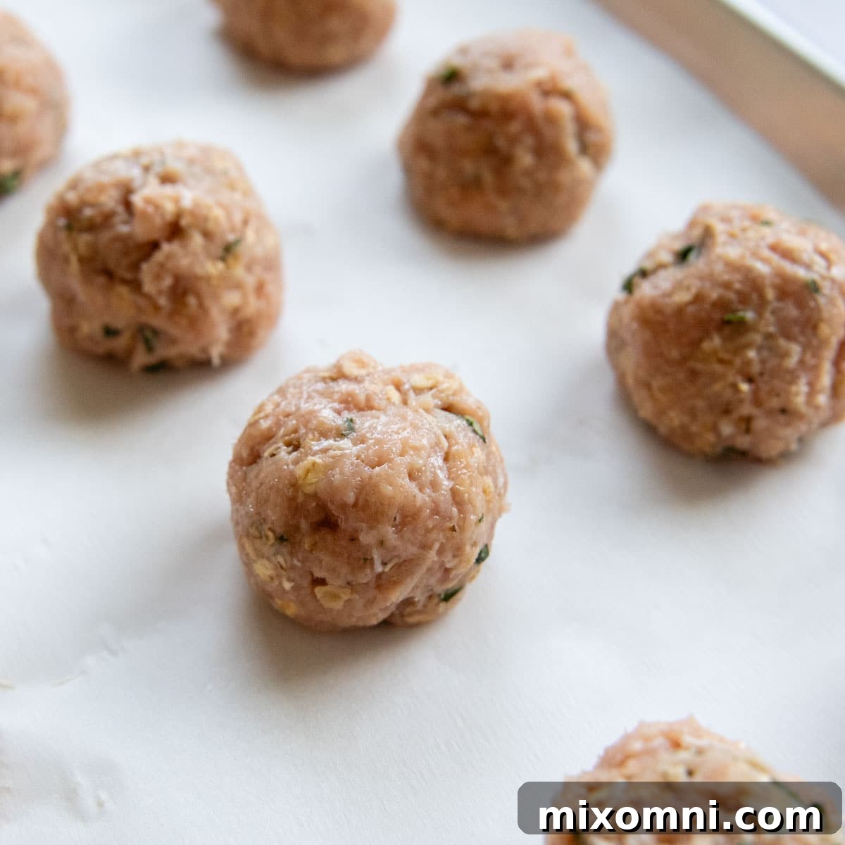 Raw, perfectly shaped chicken meatballs ready for baking, arranged neatly on a parchment-lined baking sheet.
