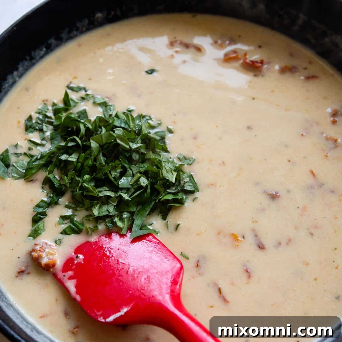 Fresh basil being stirred into the simmering creamy sun-dried tomato sauce, adding a vibrant finish.