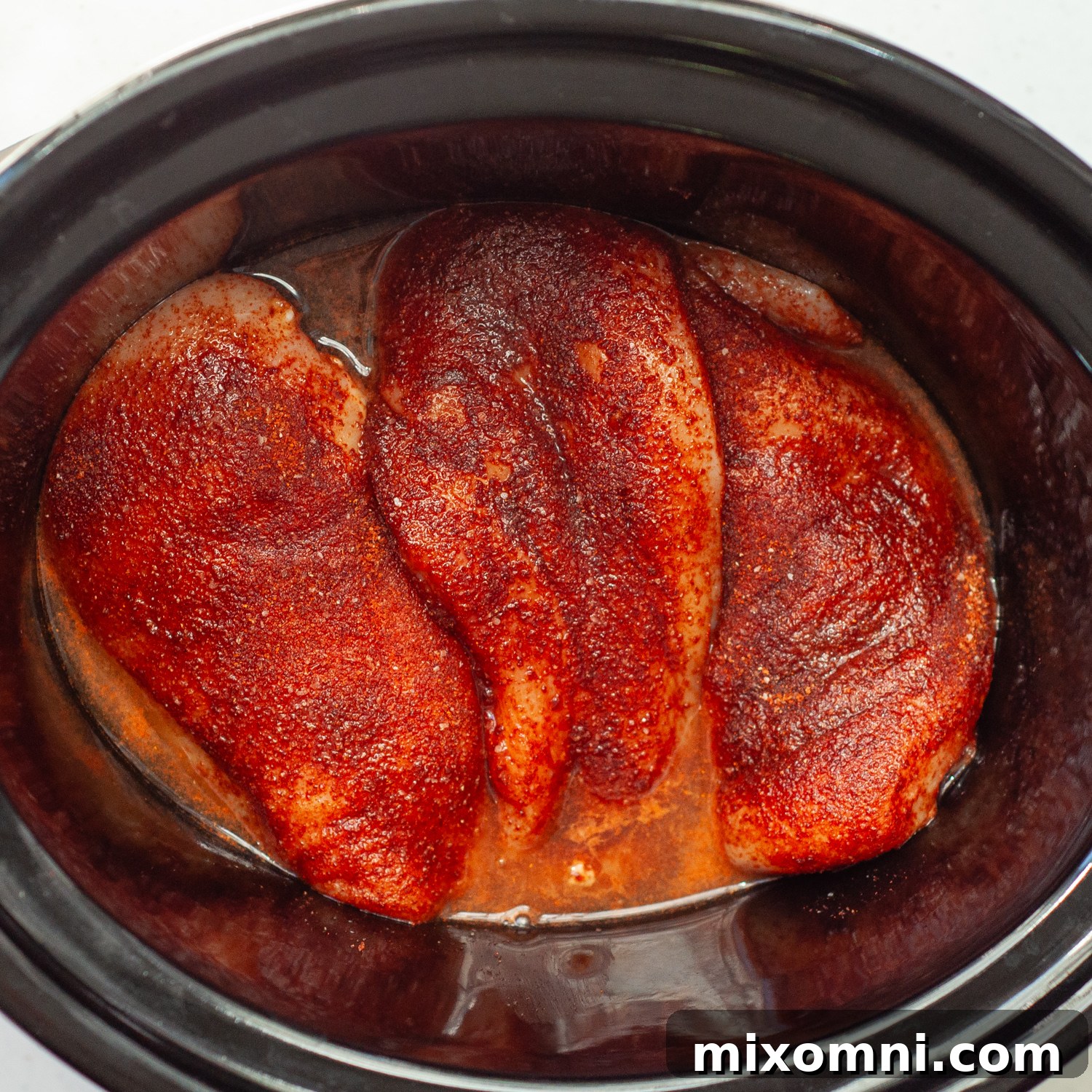 Chicken breasts generously coated with seasoning, ready to be slow-cooked to tender perfection.