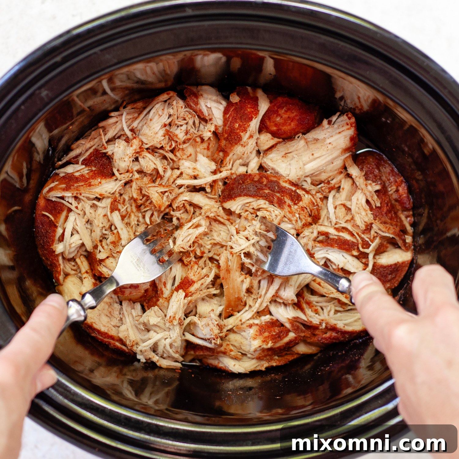 Tender chicken being shredded with two forks directly in the crock pot, creating the perfect texture for pulled chicken.