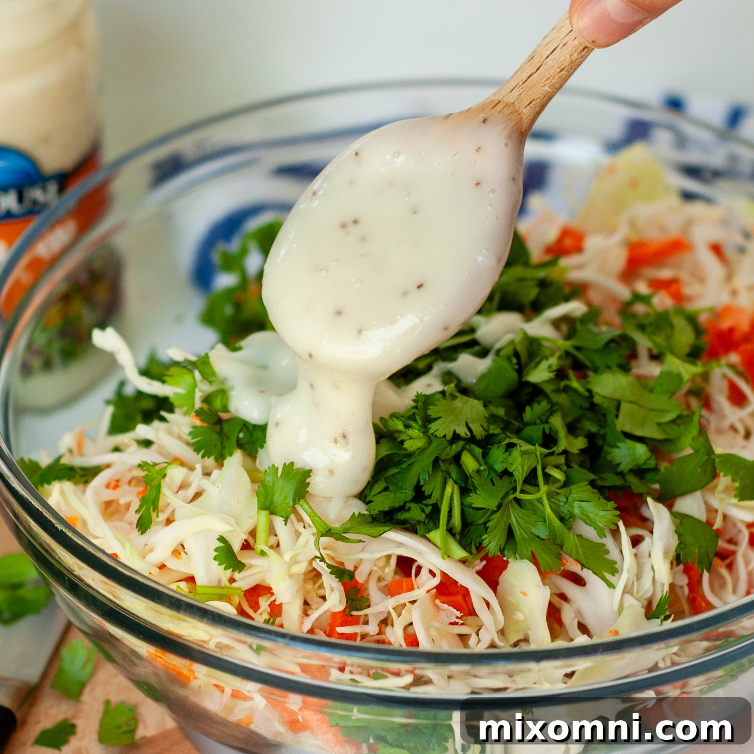 Creamy coleslaw dressing being stirred into a vibrant mix of shredded cabbage and other vegetables.