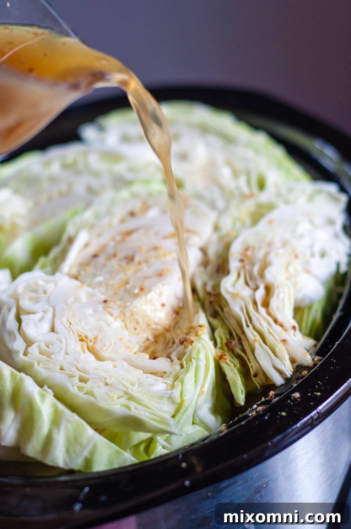 Apple juice mixture being poured over cabbage wedges nestled around a corned beef brisket in a slow cooker.