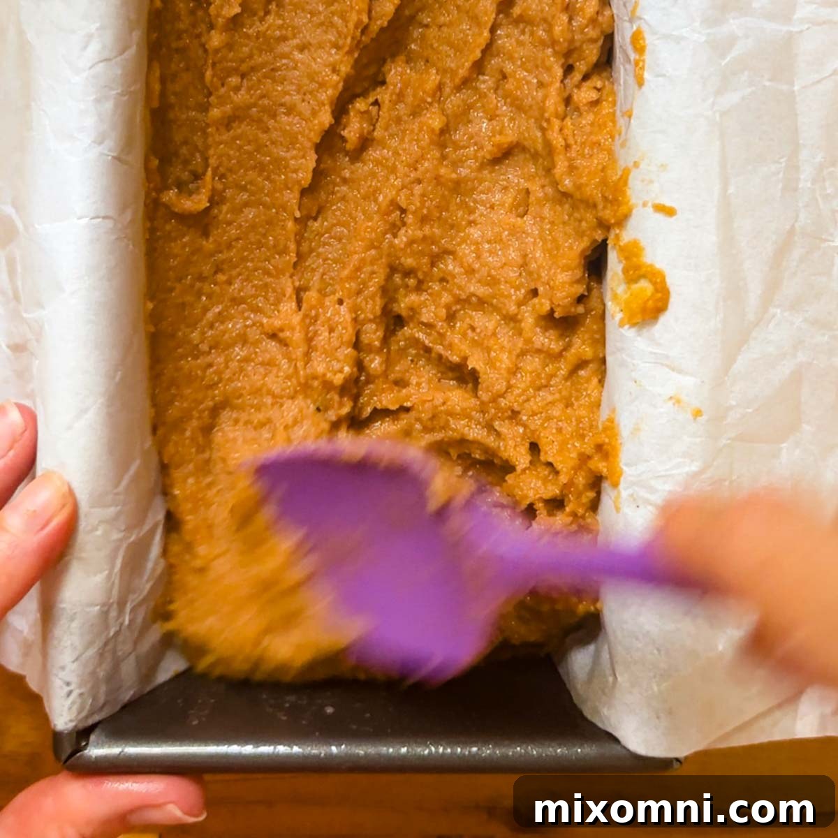Overhead shot of almond flour pumpkin bread batter being spread in a loaf pan, topped with streusel.