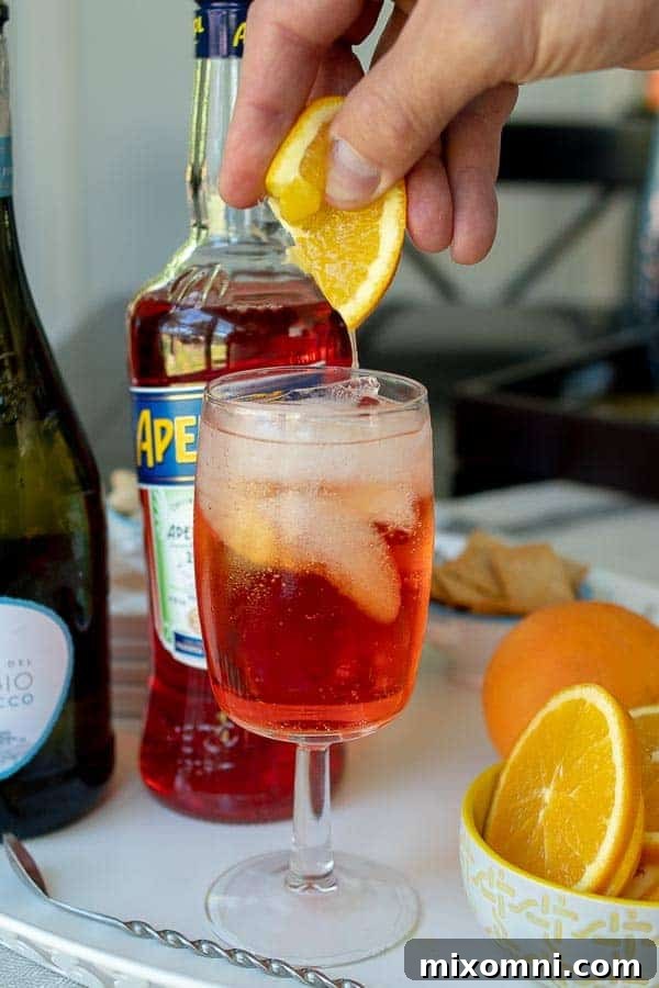 A close-up shot of a hand squeezing a fresh orange slice directly into a glass of Aperol Spritz, creating a swirl of citrus and effervescence.