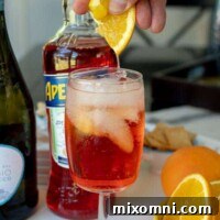 A freshly prepared Aperol Spritz cocktail, with a hand squeezing a fresh orange slice into the glass, highlighting the vibrant colors and bubbles.