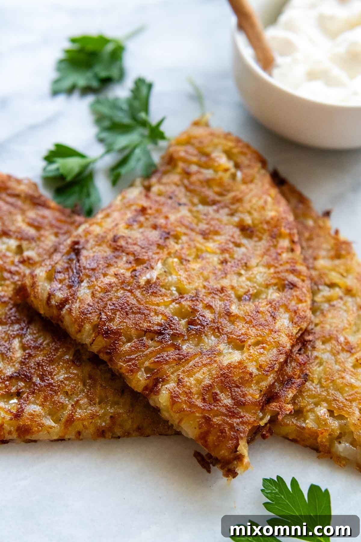 A perfectly cooked Swiss potato rösti, sliced into a wedge and elegantly plated with a fresh parsley garnish, showcasing its golden crust and fluffy texture.