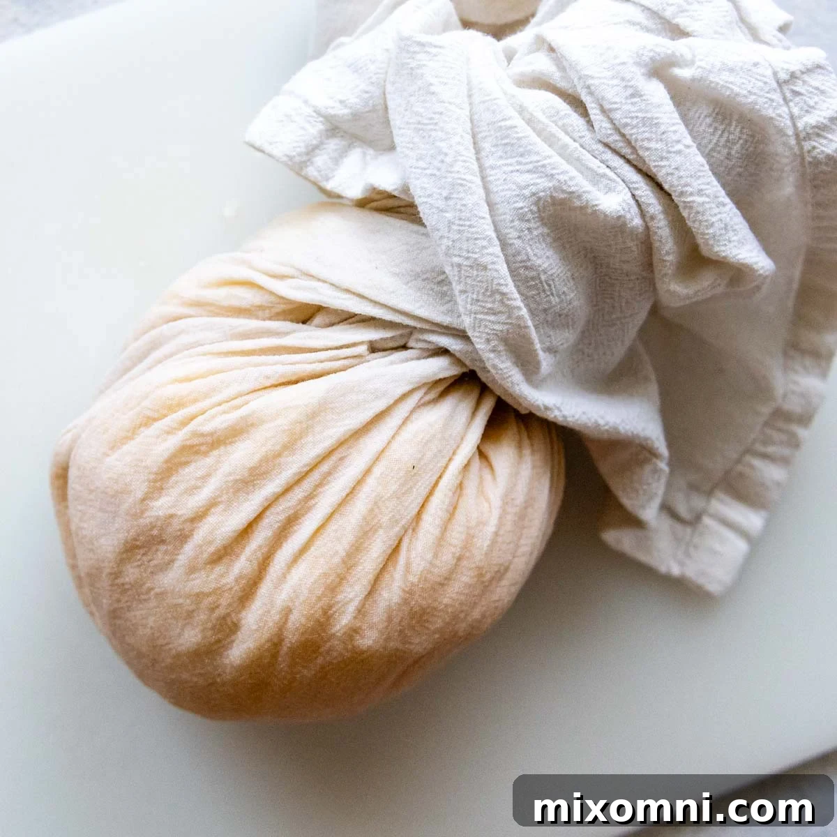Hands firmly squeezing grated potatoes wrapped in a white kitchen towel, demonstrating the crucial step of removing excess moisture.