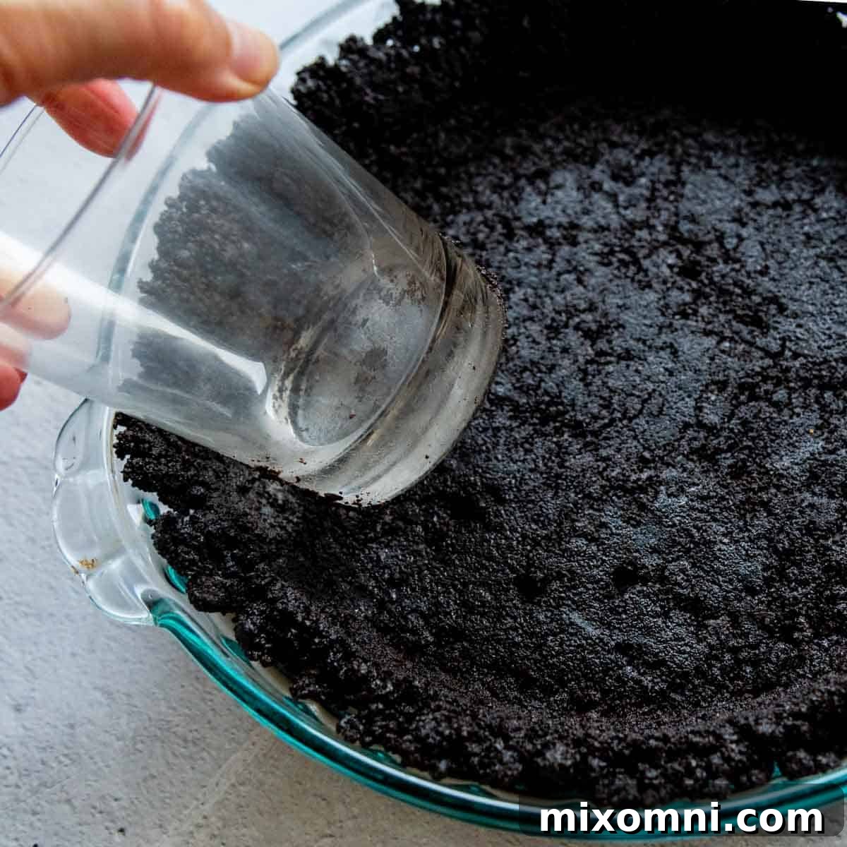 The edges of the Oreo crust are carefully shaped and pressed upwards along the pie dish using the side of a drinking glass.