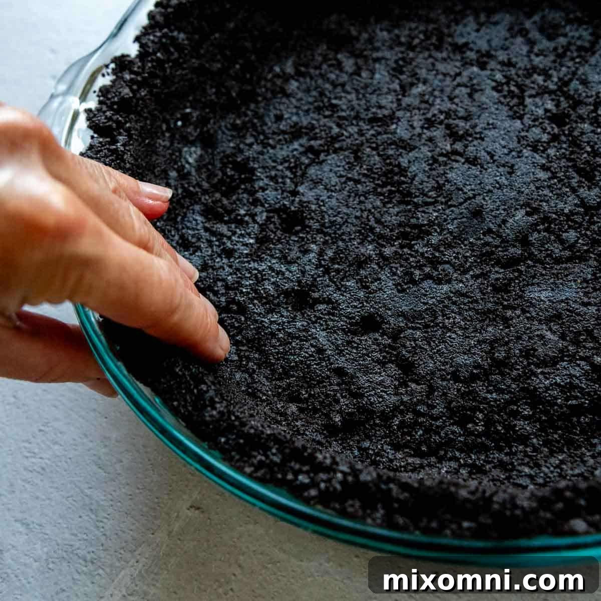 The side of the gluten-free Oreo crust is meticulously pressed and smoothed against the glass pie dish by hand, ensuring a clean and even edge.