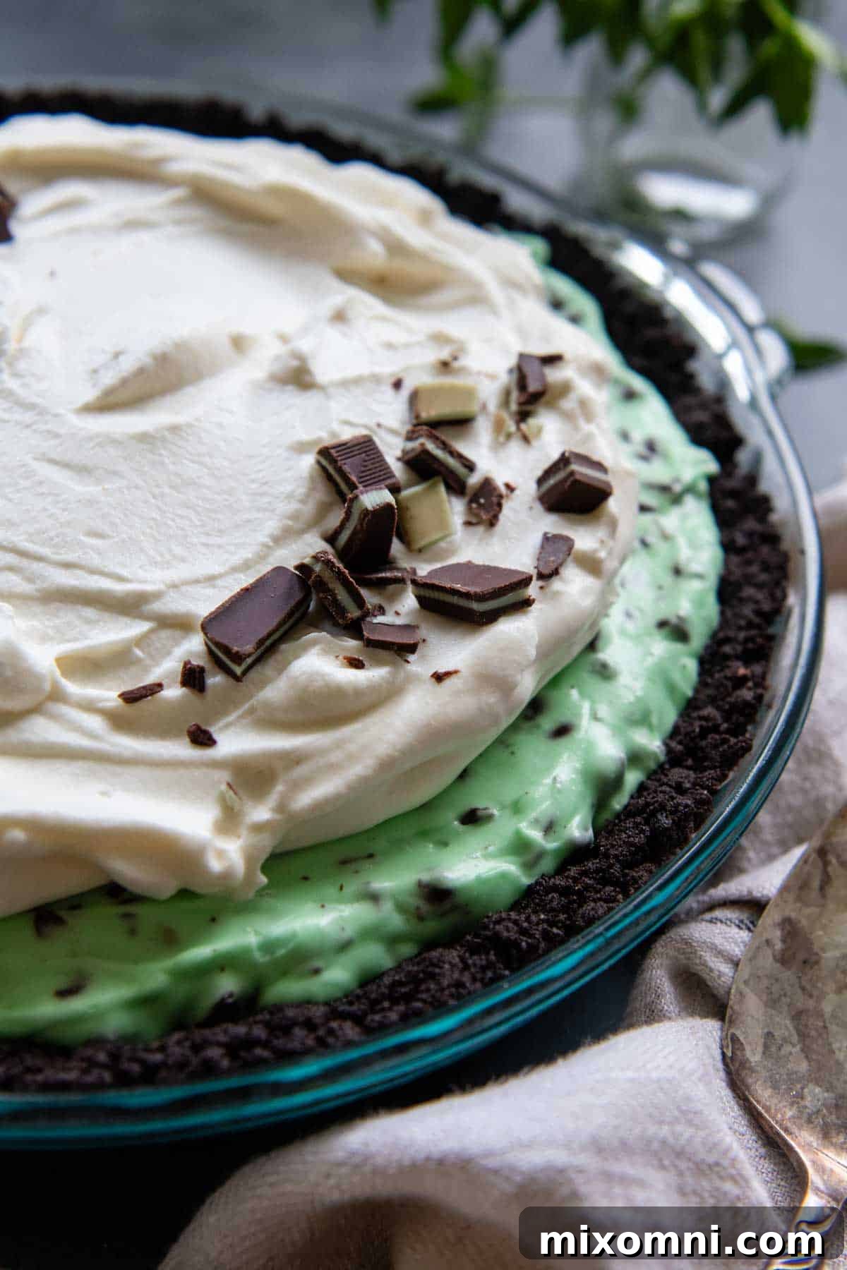 A vibrant gluten-free Oreo mint pie, topped with generous whipped cream and sprinkled with chocolate mint candies, highlighting the versatile crust.