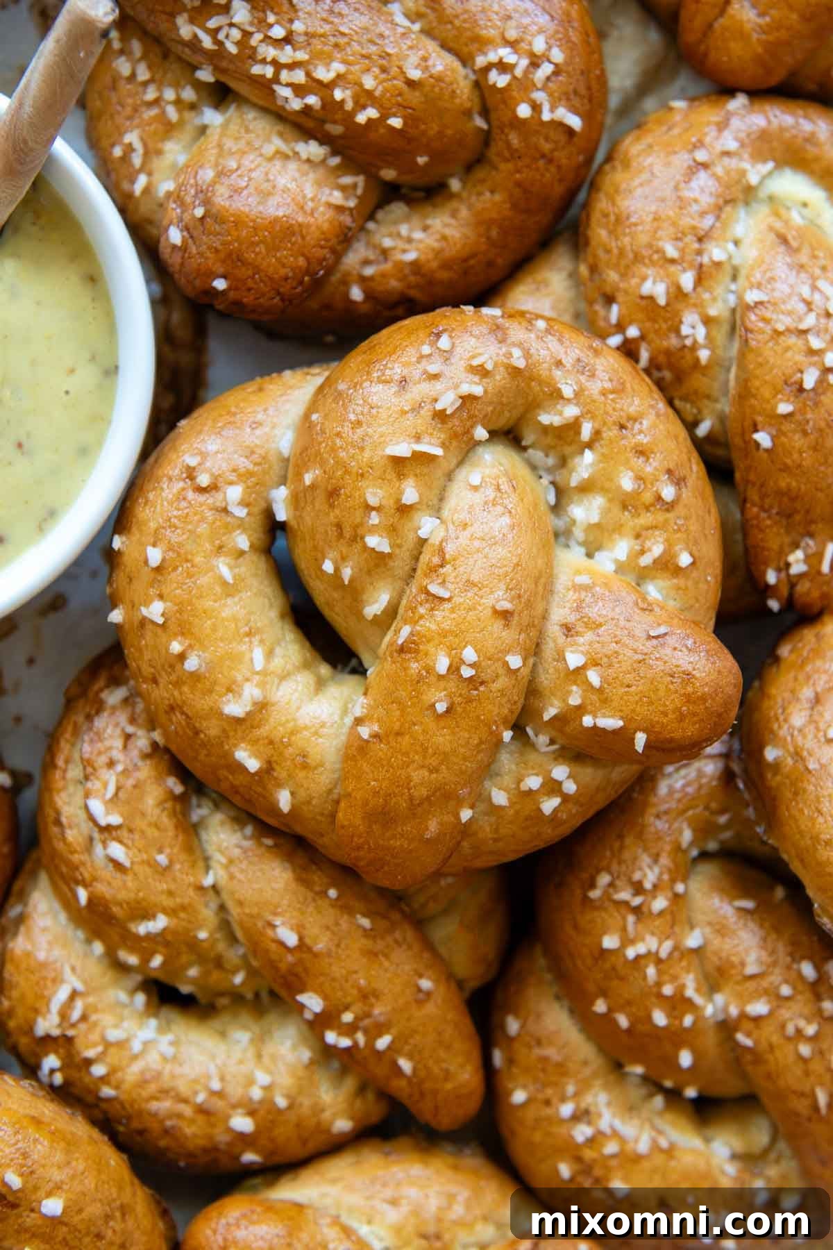 close up overhead view of a gluten-free pretzel that shows the golden brown color and the white salt flakes with a bowl of mustard dipping sauce off to the left side