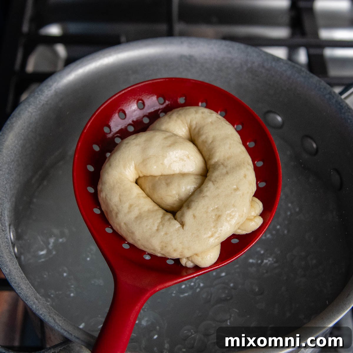 fully shaped pretzel being held in a slotted spoon being placed into a pot of boiling water.