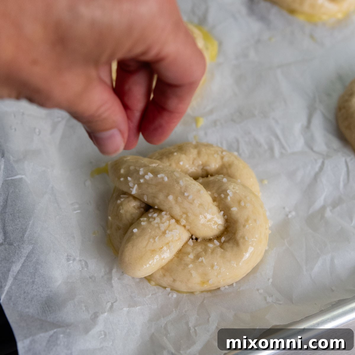 a hand sprinkling on salt to the unbaked pretzel.