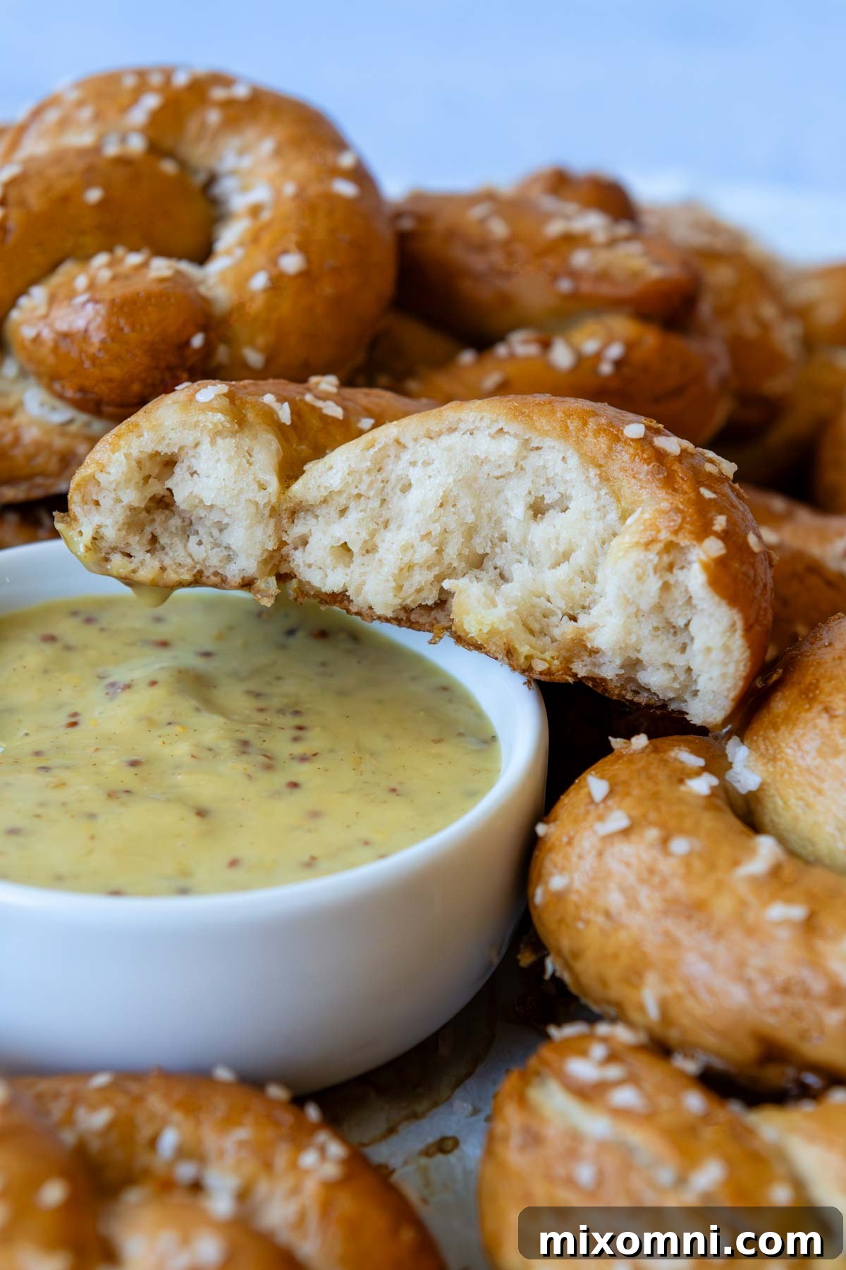 gluten-free pretzel cut open to show inside of pretzel and is ready to be dipped in a mustard sauce.