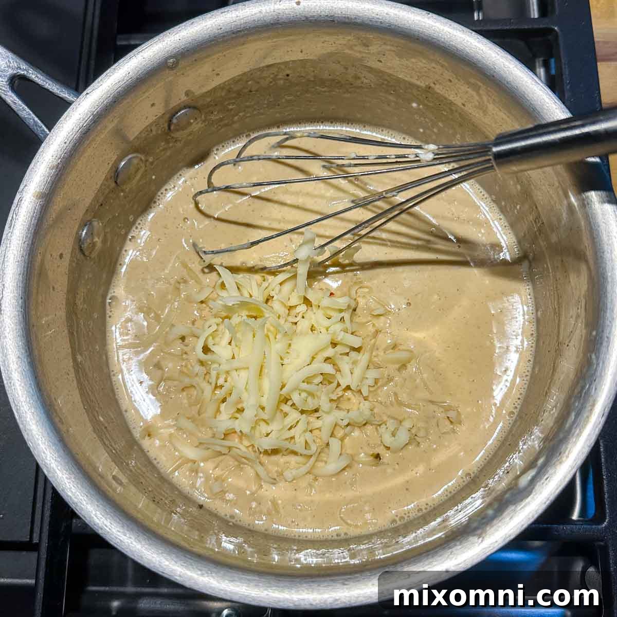 Freshly grated cheese being added gradually to the creamy milk and cream cheese mixture in a saucepan.