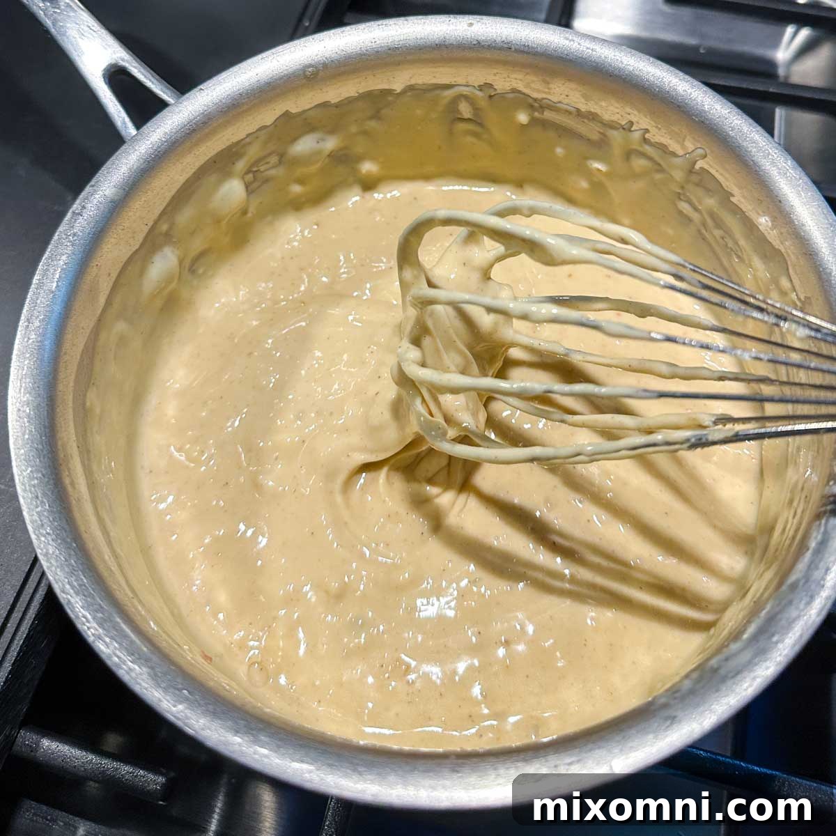 A whisk lifting out of the completed queso cheese sauce, showcasing its smooth and creamy consistency.