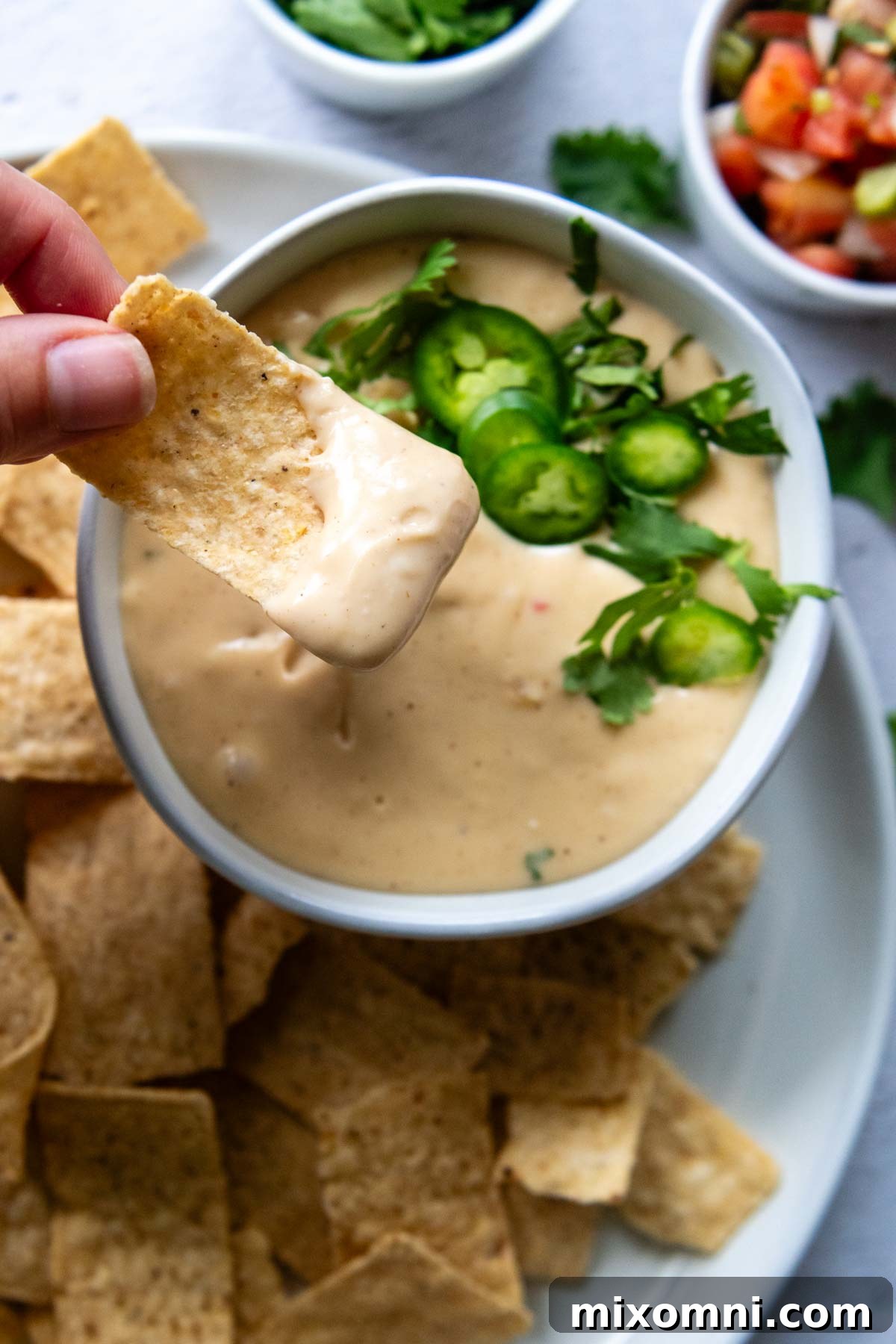A hand dipping a vibrant blue tortilla chip into a rich, golden bowl of gluten-free queso cheese sauce.