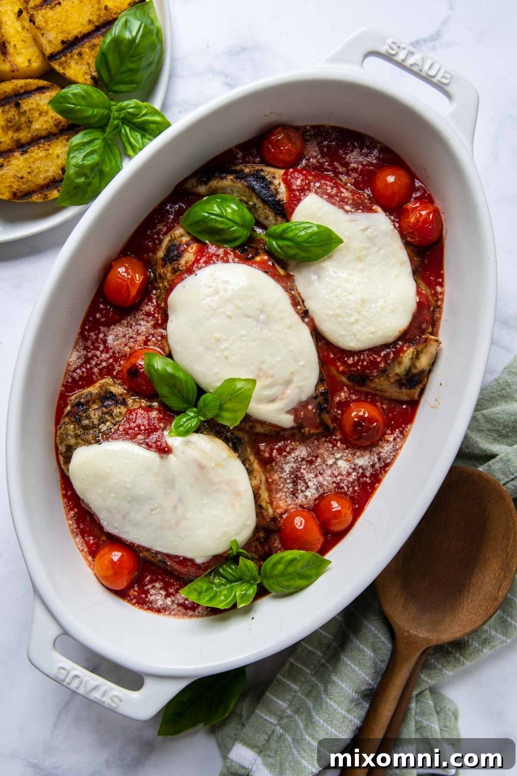 Overhead shot of grilled chicken parmesan in a white oval dish with fresh basil leaves on top, ready to serve