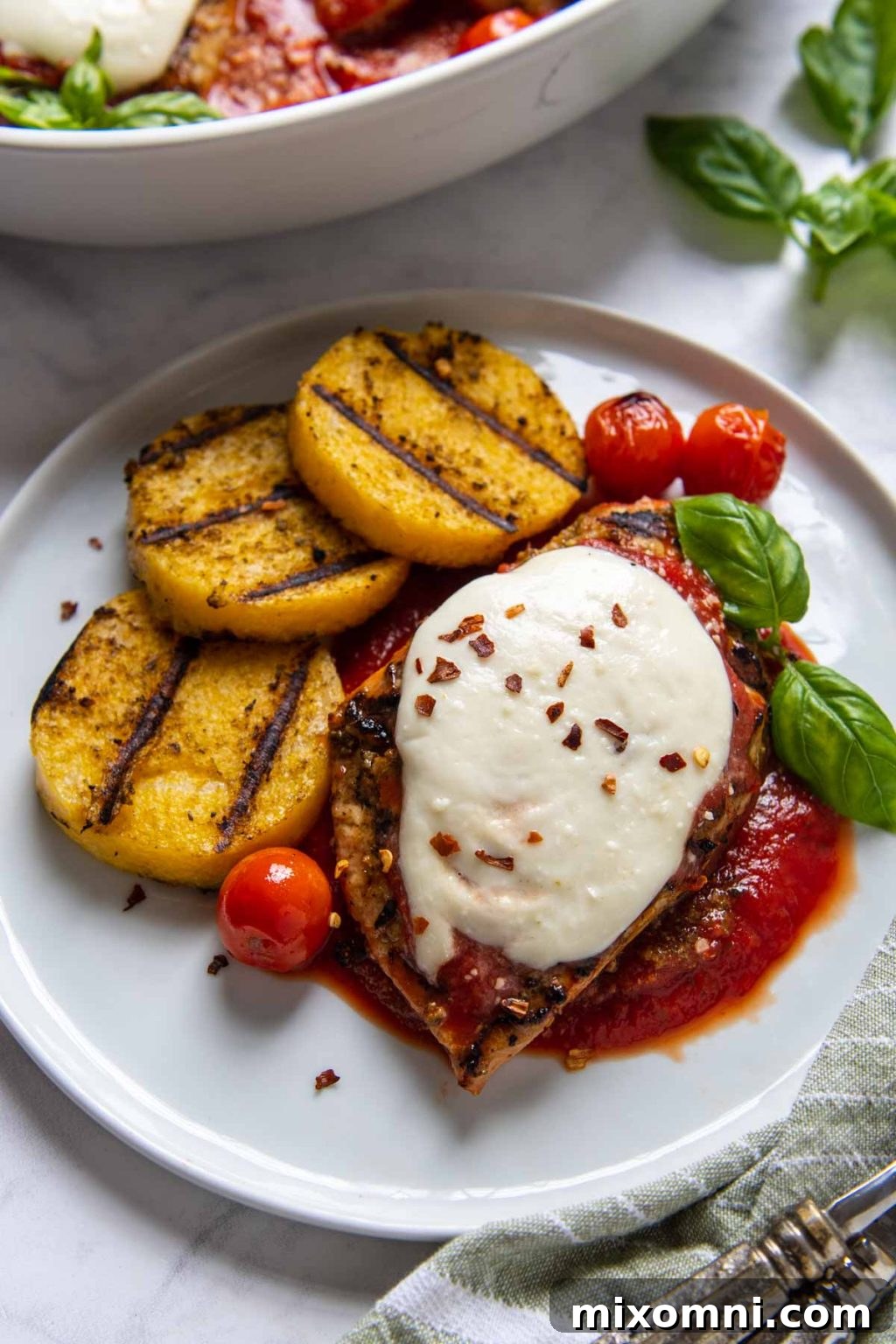 Close up of grilled chicken parmesan dinner plated with a large serving dish in the background