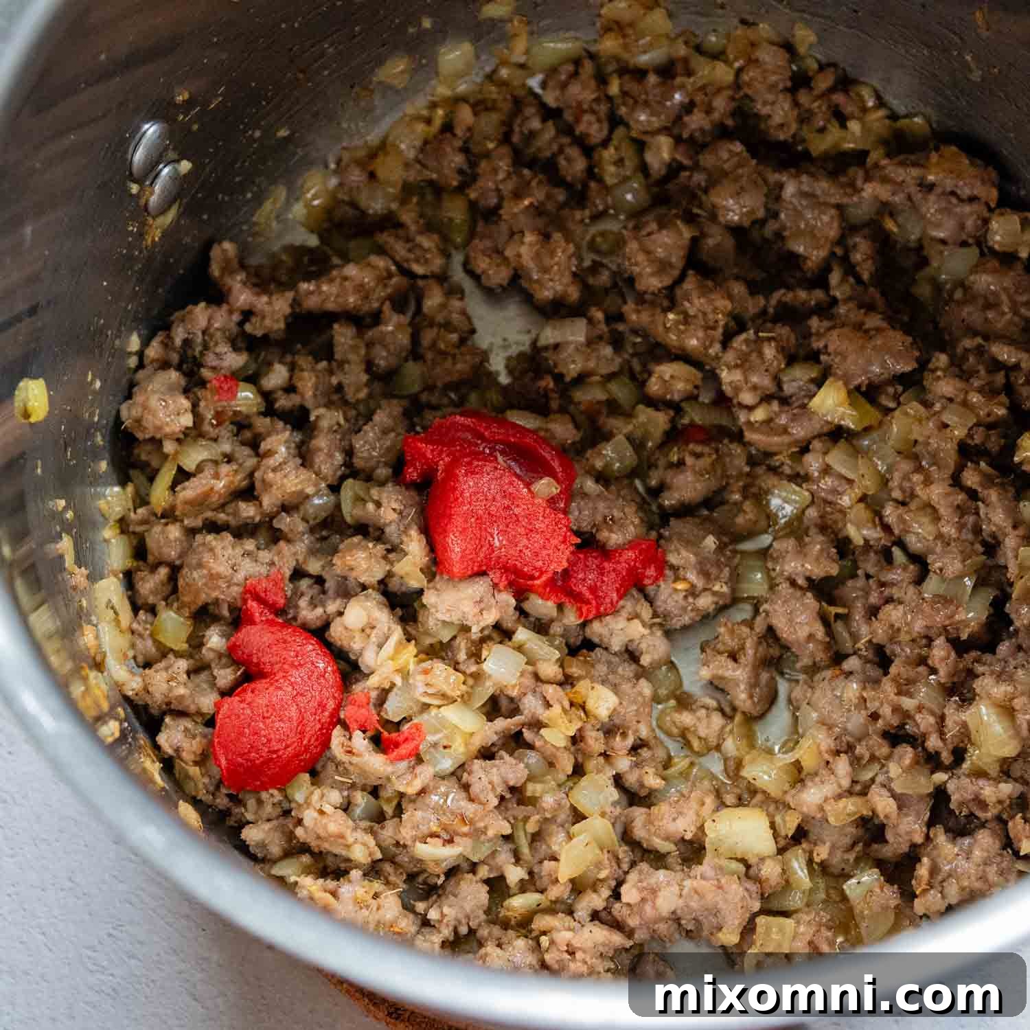 Pot of cooked sausage and a dollop of tomato paste.