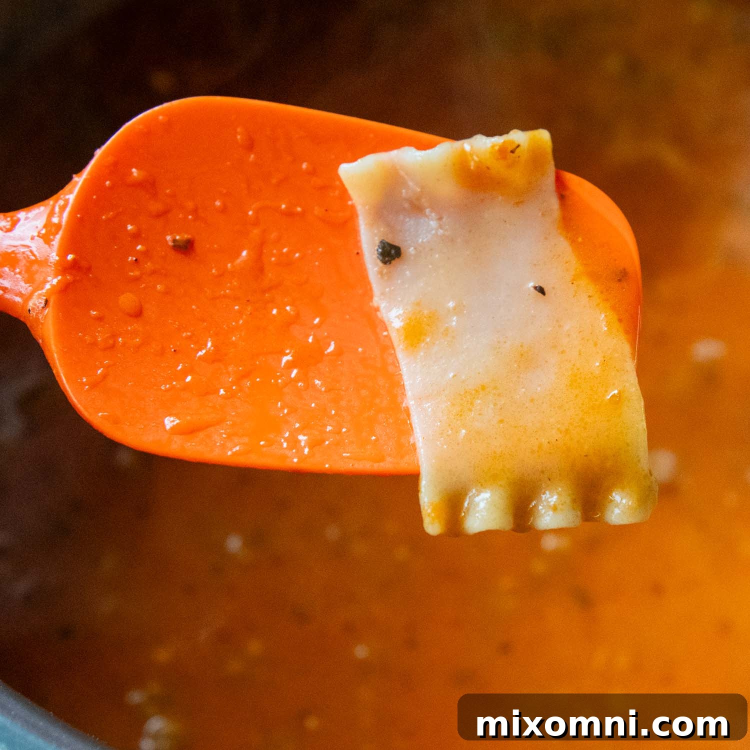 orange spoon lifting a lasagna noodle out of soup to be checked for doneness.
