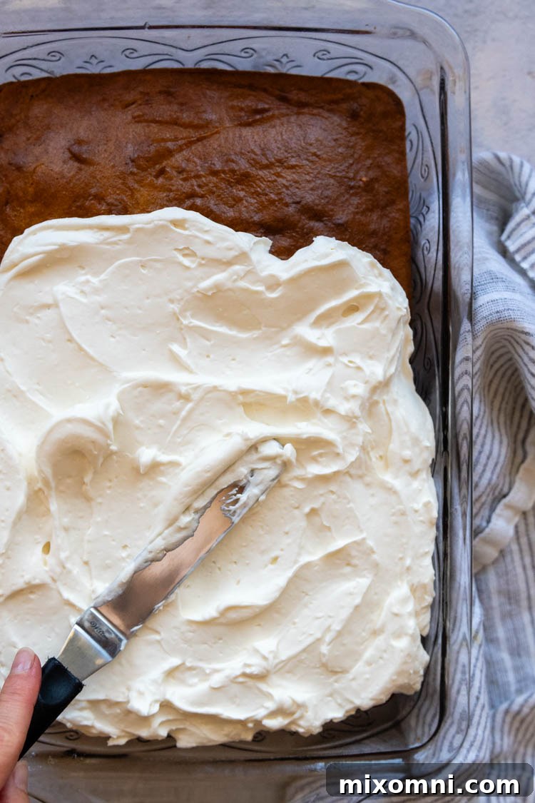 cake in glass cake pan with a knife spreading frosting on top.