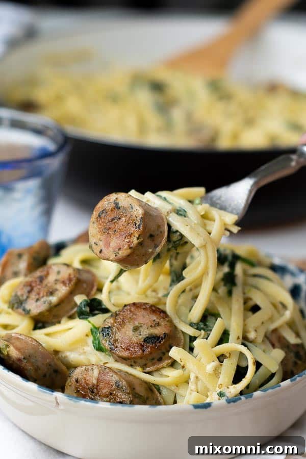A fork lifting a bite of creamy chicken sausage pasta, showcasing the fettuccine, sausage, and spinach.