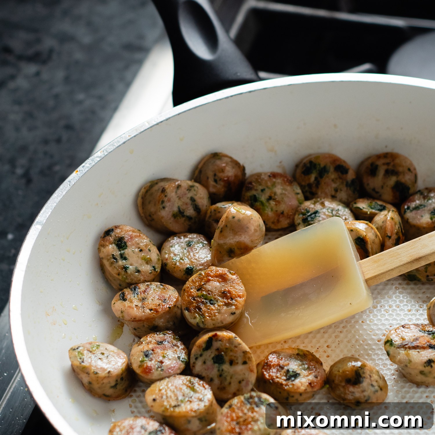 Chicken sausage medallions sizzling and browning in a skillet on the stovetop.