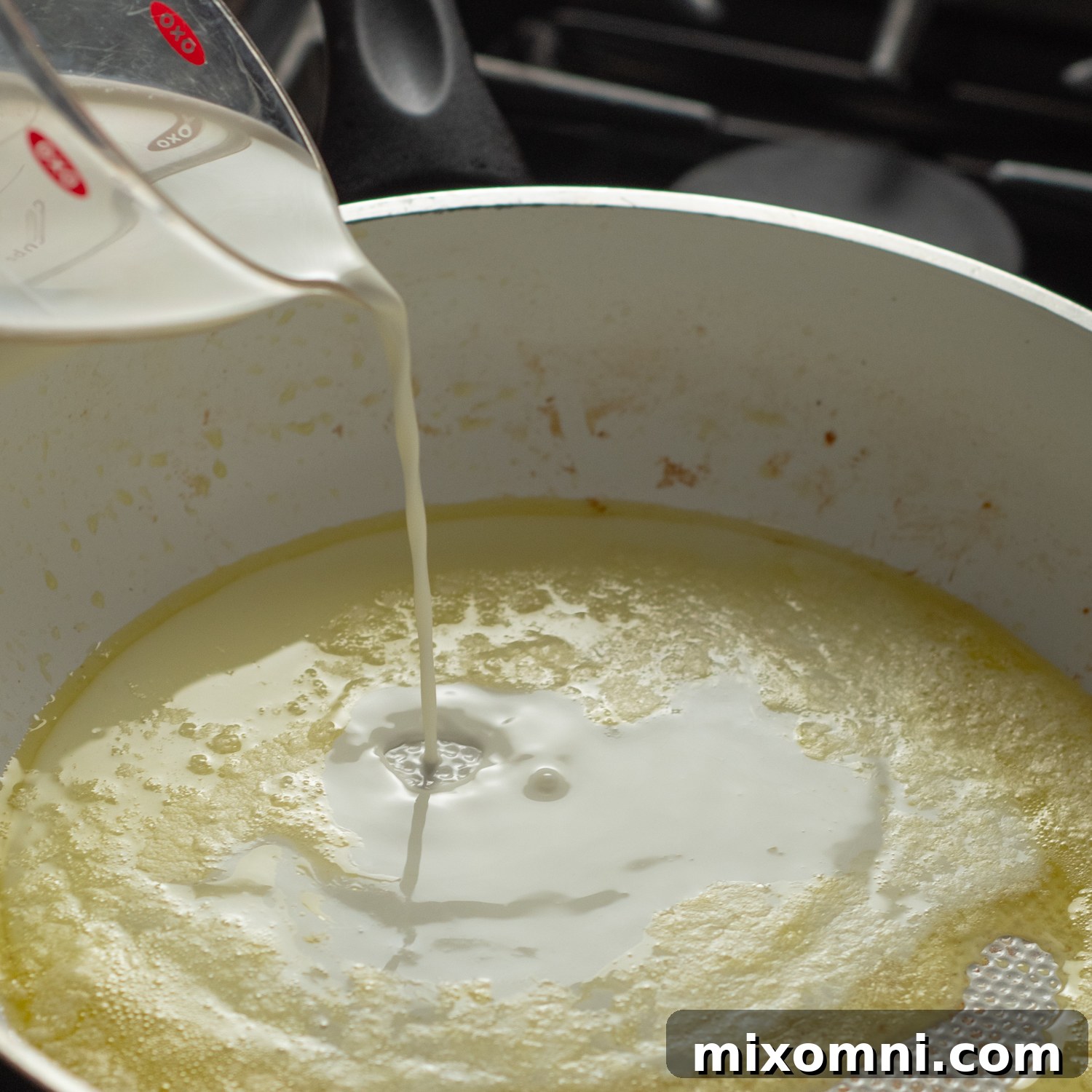 Half and half being poured into a skillet, forming the base of the creamy pesto sauce.