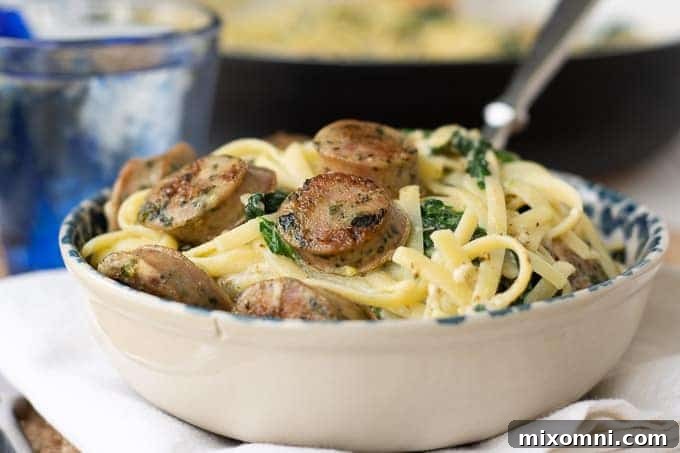 A bowl of creamy chicken sausage pasta with a fork going in for a bite, garnished with fresh herbs.