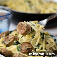 A fork lifting up a bite of creamy chicken sausage pasta from a bowl.