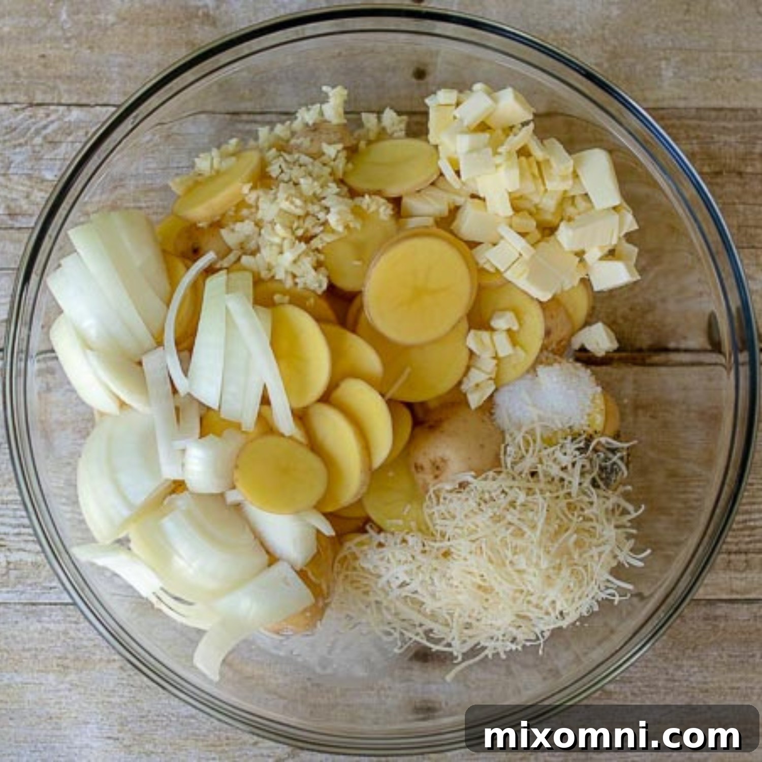 All the grilled potato ingredients, including sliced potatoes, onions, garlic, butter, cream, and parmesan cheese, are mixed in a large bowl, ready for seasoning.