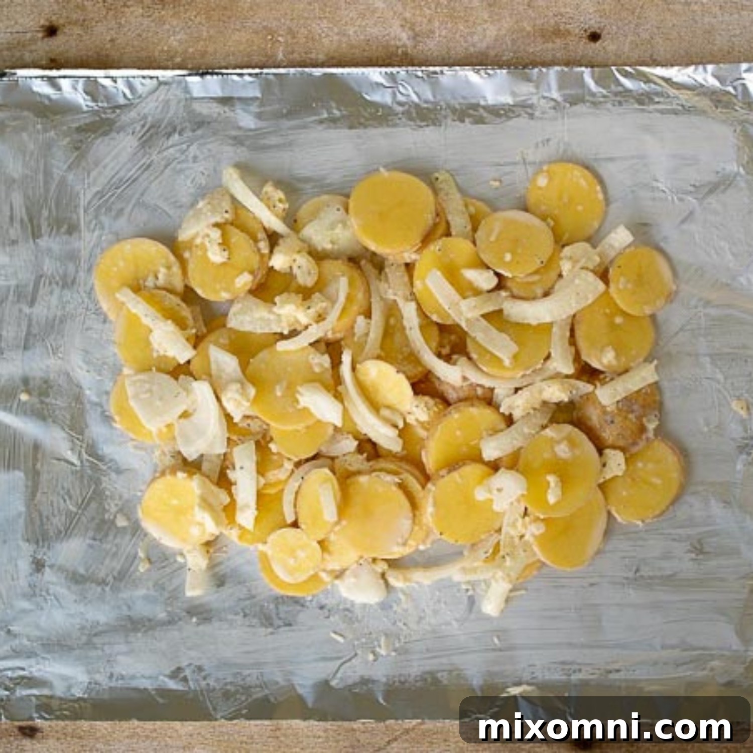 Thinly sliced potatoes and onions are spread evenly on a greased sheet of aluminum foil, ready to be wrapped into a packet.