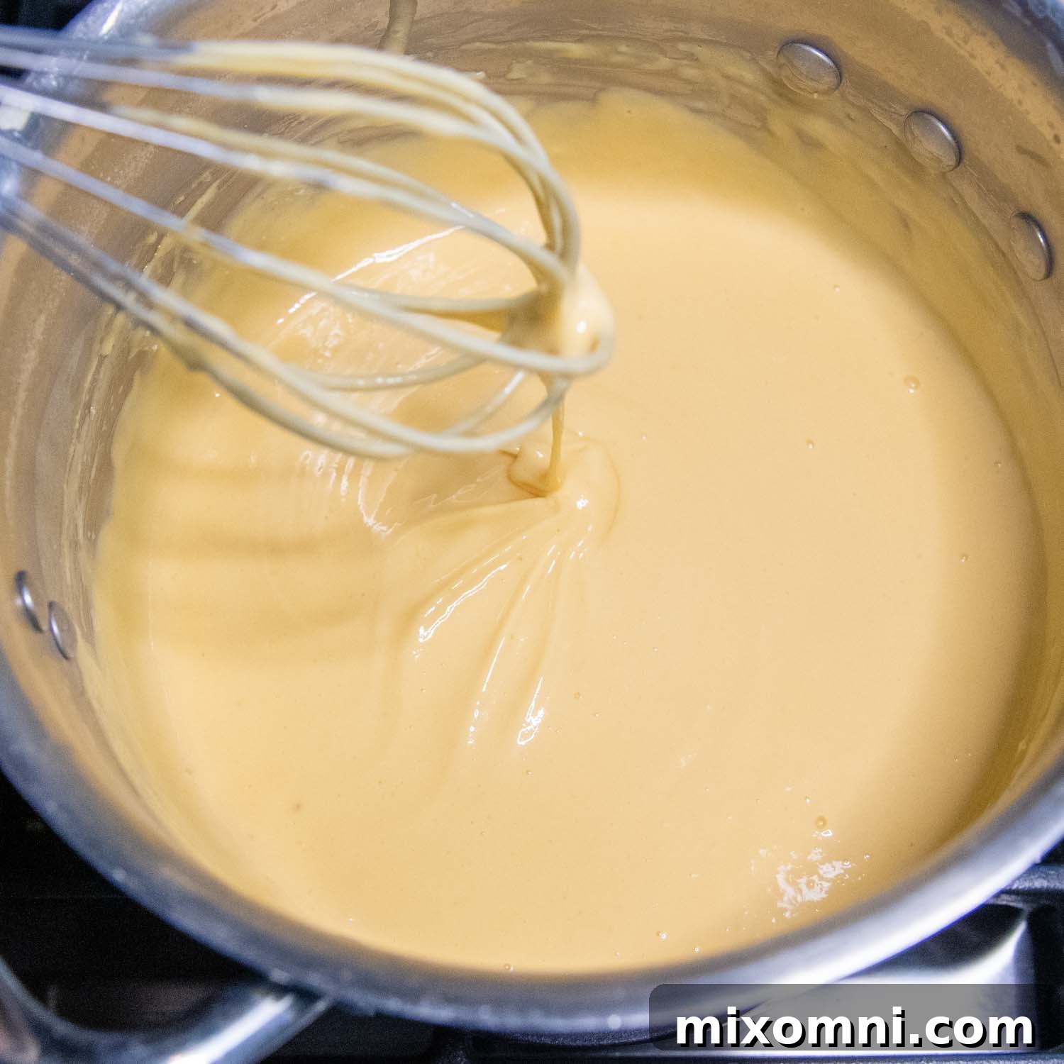 Whisking cheese into other ingredients in a sauce pan, creating a smooth sauce.
