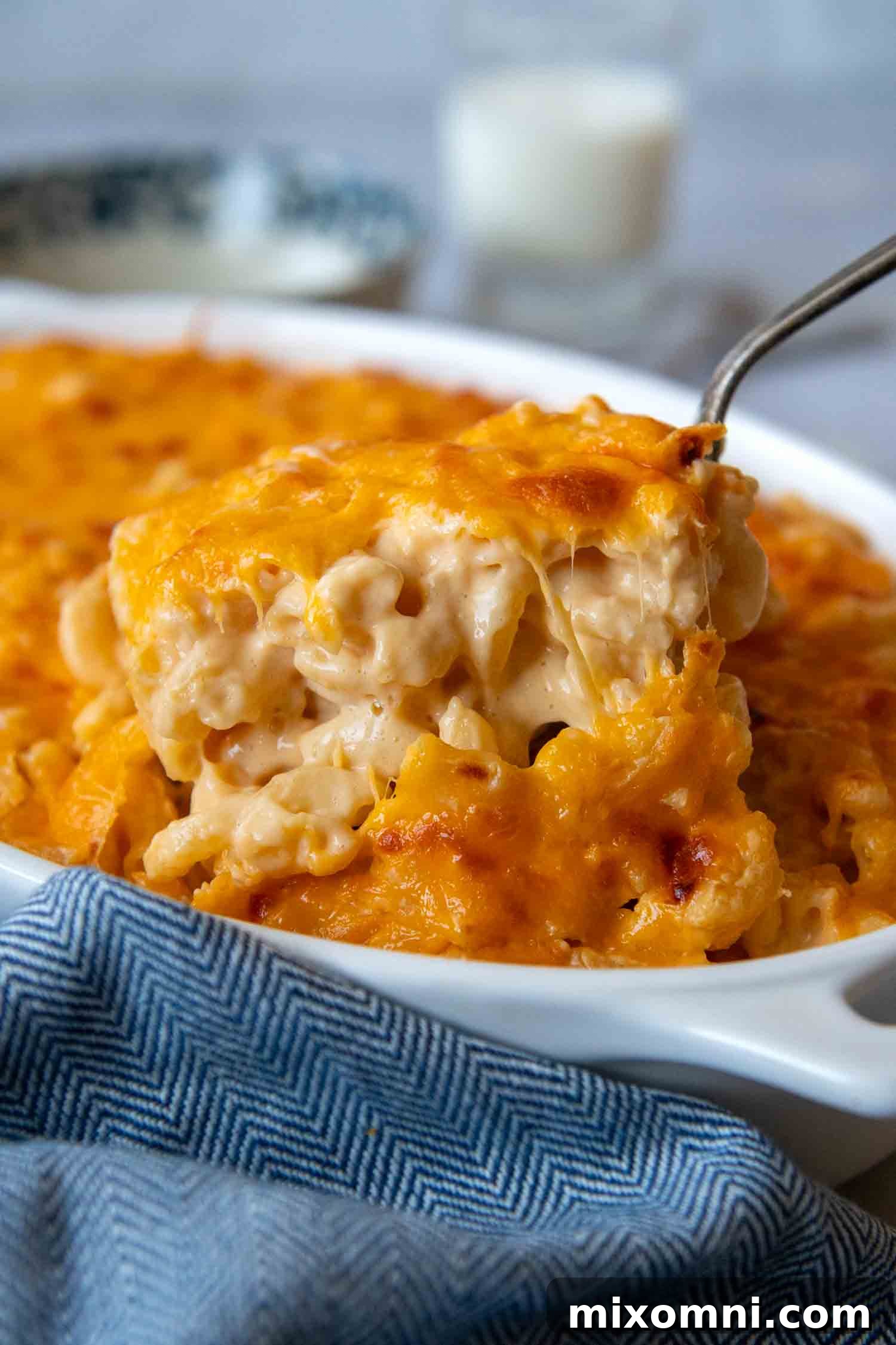 Mac and Cheese being lifted out of a white baking dish with a spoon, demonstrating its rich, gooey cheesiness.