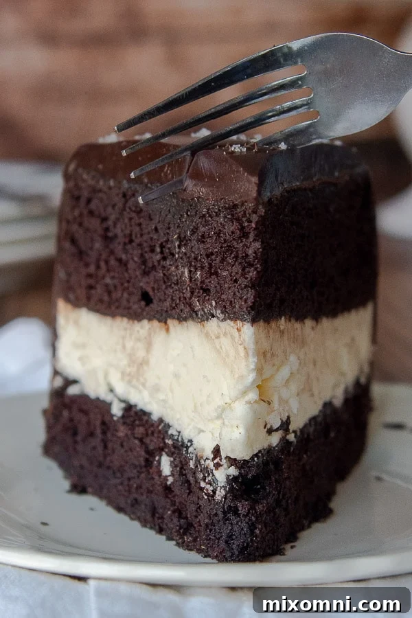 A fork sinking into a luscious slice of homemade Ding Dong cake, revealing layers of chocolate cake, fluffy cream filling, and shiny ganache.