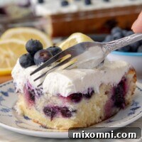 a fork cutting into a piece of lemon blueberry cake on a white plate with fresh blueberries on top