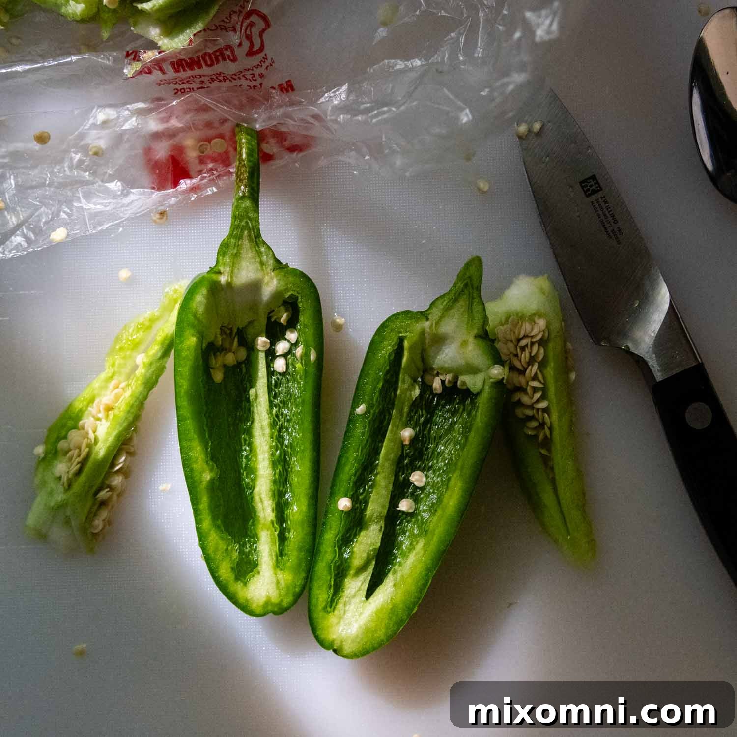 A fresh jalapeño pepper on a cutting board, sliced in half, with some seeds still visible, next to a knife.