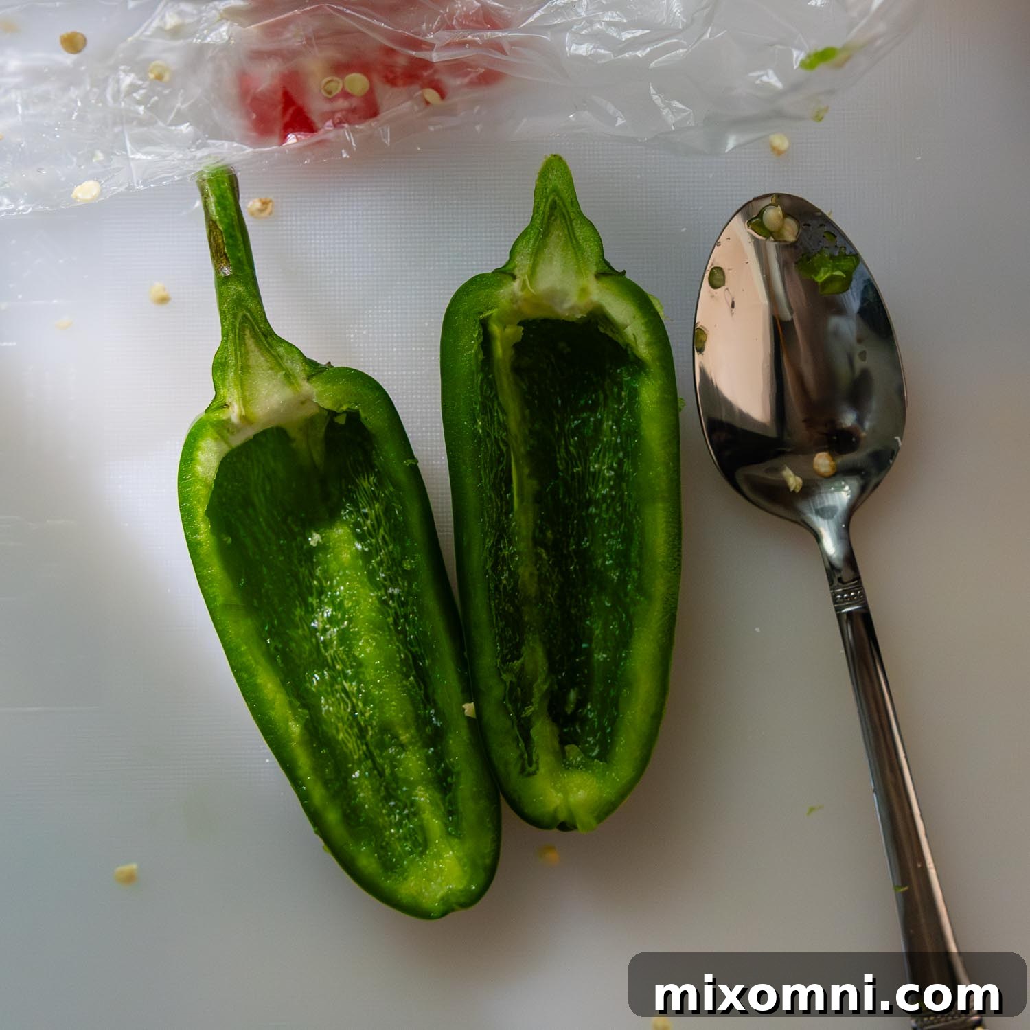 A halved jalapeño pepper on a cutting board with seeds and membrane removed using a small spoon, showcasing a clean cavity.