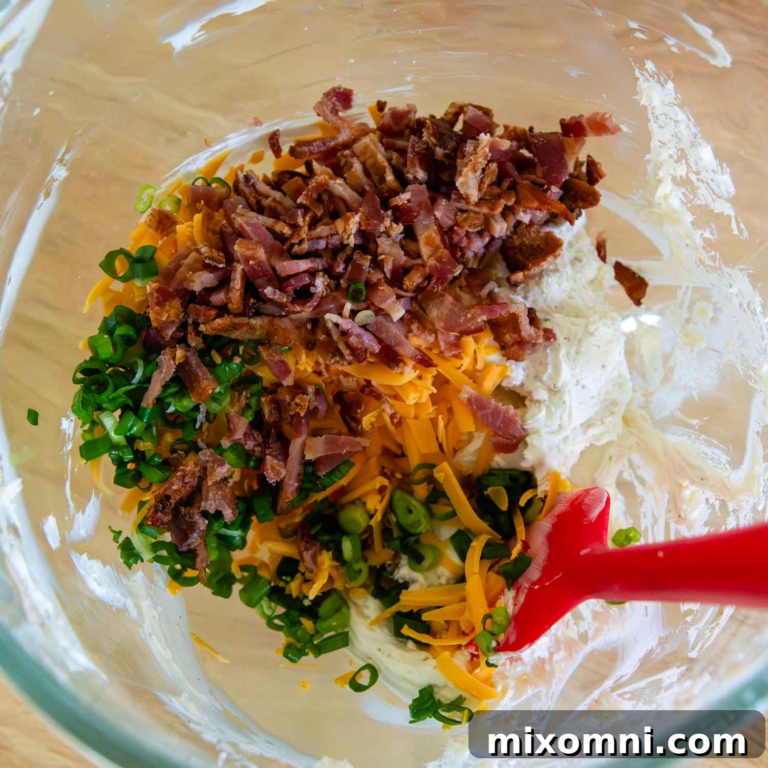 A glass bowl filled with the creamy, cheesy jalapeño popper mixture, showing bits of bacon, green onion, and cheddar cheese.