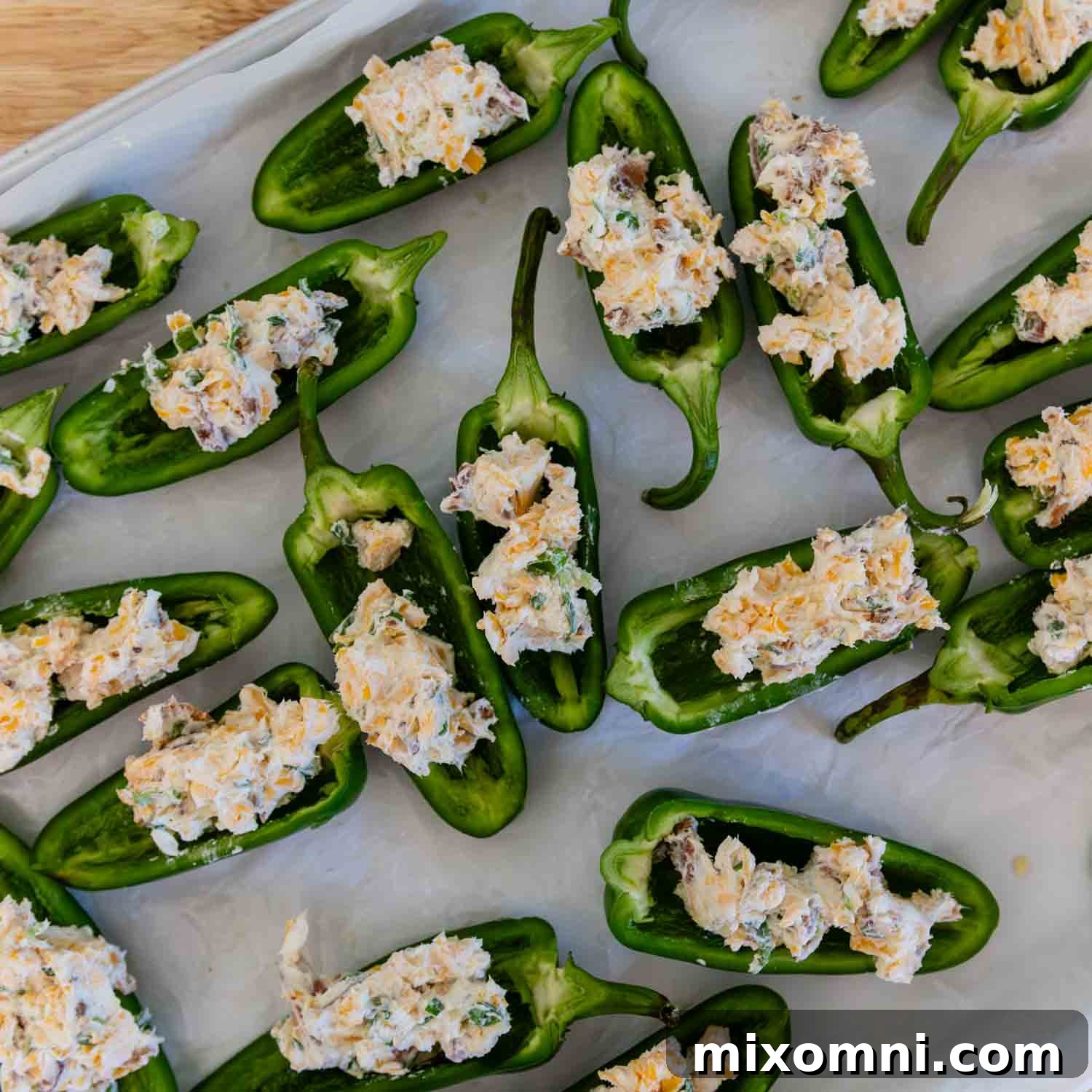 Prepared jalapeño halves lined on a baking sheet, generously filled with the cream cheese and bacon mixture.