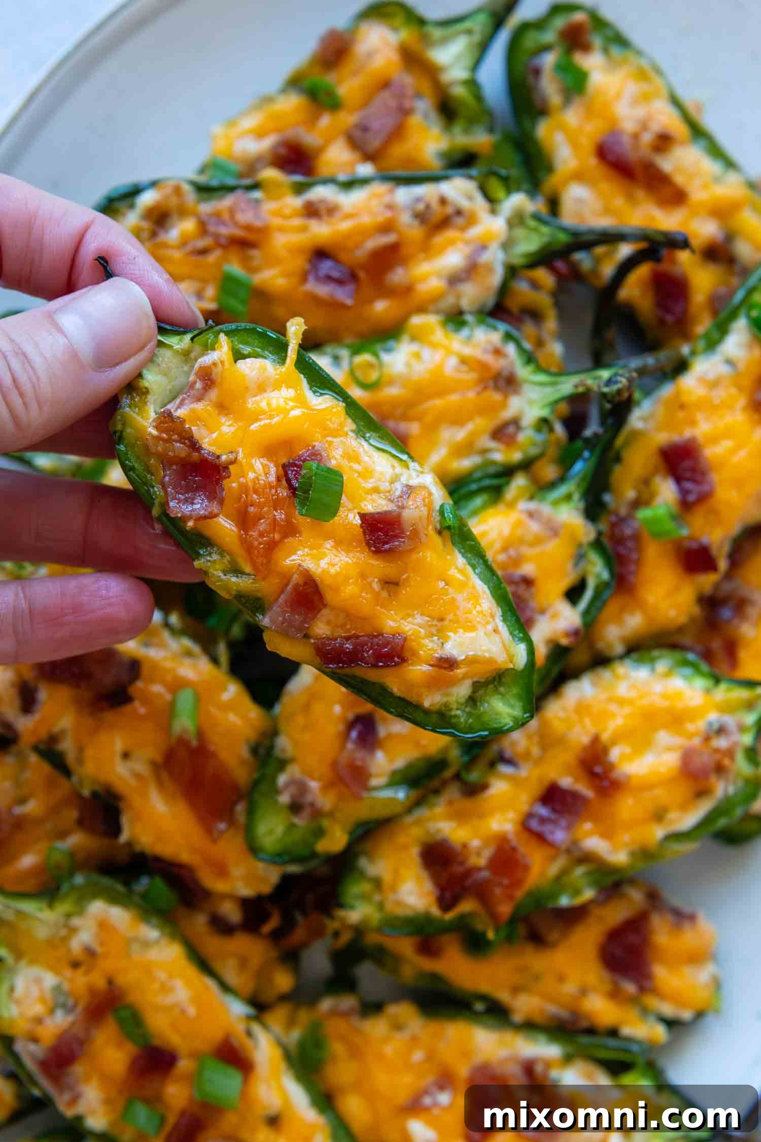 A hand carefully holding a perfectly baked gluten-free jalapeño popper, showcasing its golden topping.