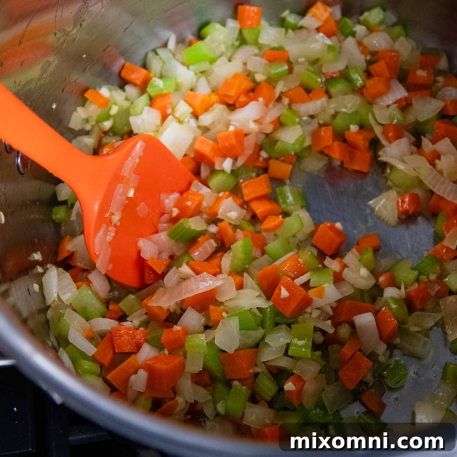 Dutch oven with onions, carrots, and celery being sautéed in olive oil.
