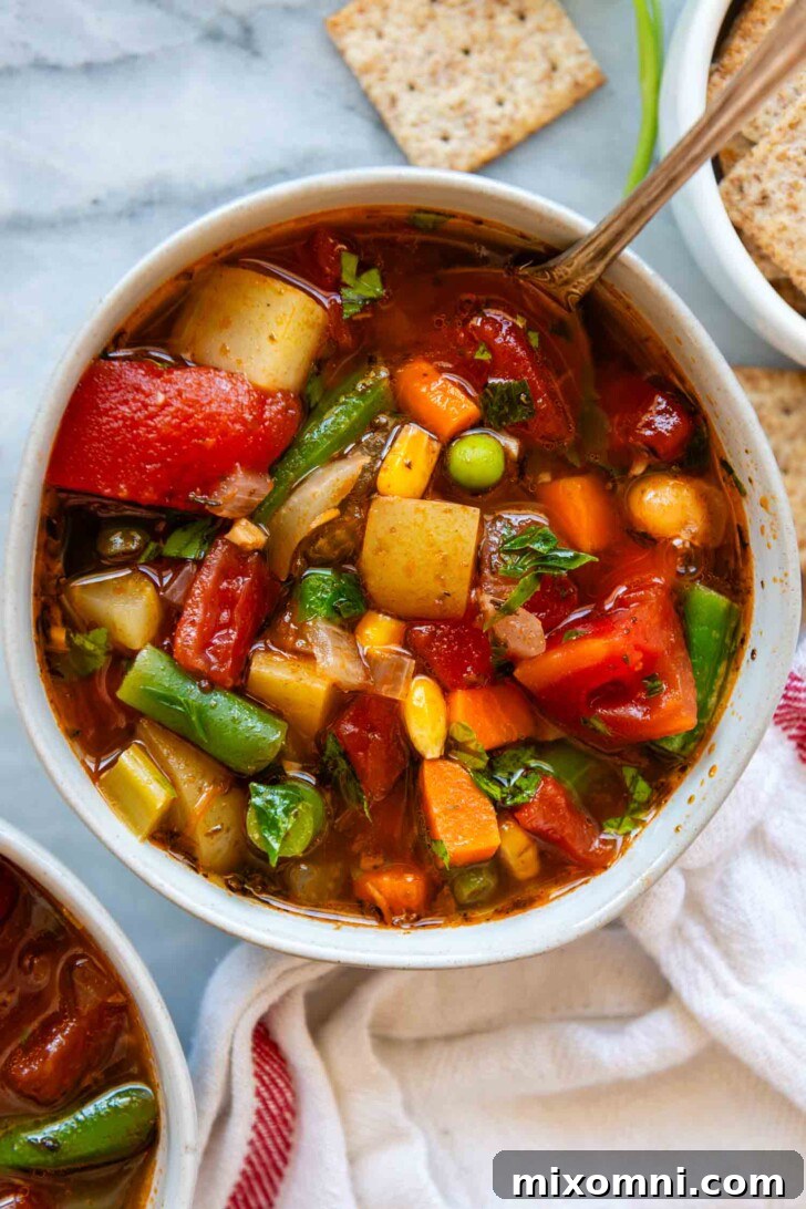 Overhead shot of a white bowl filled with chunky homemade vegetable soup, garnished with fresh parsley.