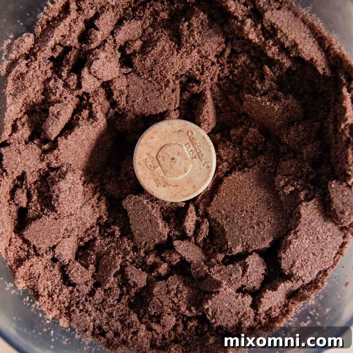 Food processor filled with finely processed dry cookie ingredients, including almond flour, chocolate, sugar, and spices.